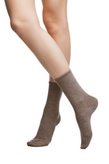 Cropped shot of a girl's cross legs, staying on a white background. It is grey socks on her foots. 