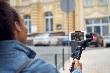Outdoors Leisure. Young girl blogger walking with stabilizer recording vlog on smartphone talking to camera joyful back view close-up