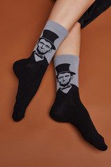 Cropped shot of a girl's foots, lying on a brown background. It is grey artwork socks with Abraham Lincoln print on foots. 