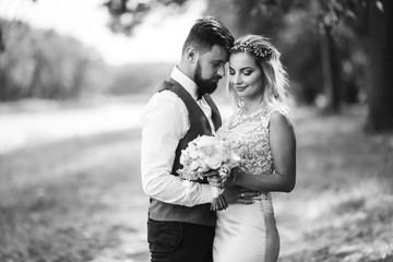 Sensual Black and white foto of bride and groom. Stylish couple of happy newlyweds posing and kisses in the park on their wedding day. Together. The concept of youth, love, fashion and lifestyle. 