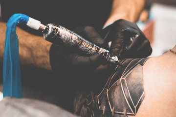 Tattoo salon. The tattoo master is tattooing a man on his shoulder. Tattoo machine, safety and hygiene at work. Close-up, tinted, tattooist