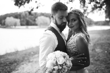 Sensual Black and white foto of bride and groom. Stylish couple of happy newlyweds posing and kisses in the park on their wedding day. Together. The concept of youth, love, fashion and lifestyle. 