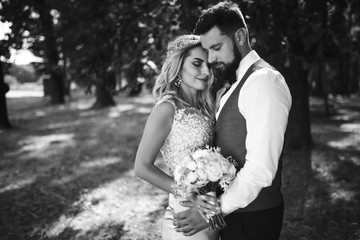 Sensual Black and white foto of bride and groom. Stylish couple of happy newlyweds posing and kisses in the park on their wedding day. Together. The concept of youth, love, fashion and lifestyle. 