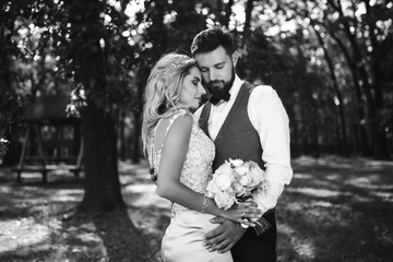 Sensual Black and white foto of bride and groom. Stylish couple of happy newlyweds posing and kisses in the park on their wedding day. Together. The concept of youth, love, fashion and lifestyle. 