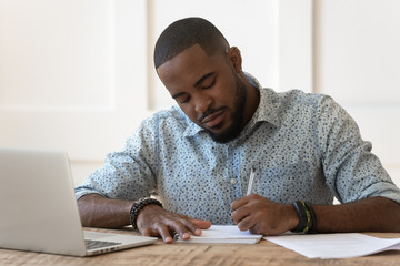 Focused african American male studying at laptop making notes © fizkes