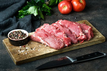 Fresh raw beef, cut into steaks  with vegetables, herbs and spices on a wooden board on a dark background.