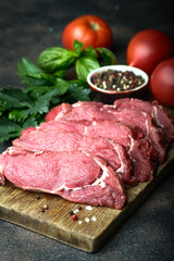 Fresh raw beef, cut into steaks  with vegetables, herbs and spices on a wooden board on a dark background.