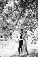 Fototapeta premium Sensual Black and white foto of bride and groom. Stylish couple of happy newlyweds posing and kisses in the park on their wedding day. Together. The concept of youth, love, fashion and lifestyle. 