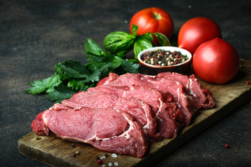 Fresh raw beef, cut into steaks  with vegetables, herbs and spices on a wooden board on a dark background.