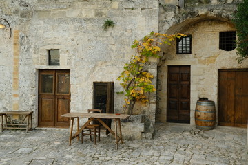 Fototapeta na wymiar Vine plant grown in a stone planter in the Sassi of Matera. Courtyard of a house with a wooden table and a wine barrel.