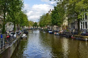Obraz premium Amsterdam, Holland. August 2019. Classic view of a canal in the city: moored boats, the tree-lined avenue with bikes, the bridges that cross the canal.