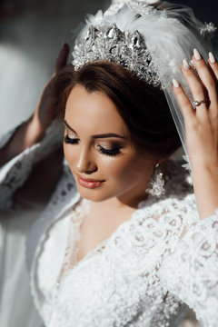 Beautiful bride portrait wedding makeup and hairstyle, girl in diamonds tiara and marriage robe, fashion bride gorgeous beauty, smiling happy bride portrait. The bride touches the crown