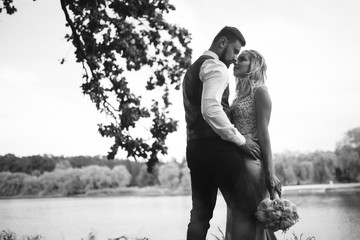 Sensual Black and white foto of bride and groom. Stylish couple of happy newlyweds posing and kisses in the park on their wedding day. Together. The concept of youth, love, fashion and lifestyle. 