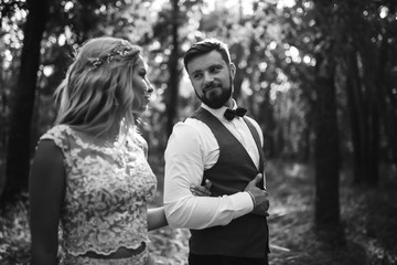 Fototapeta premium Sensual Black and white foto of bride and groom. Stylish couple of happy newlyweds posing in the park on their wedding day. Handsome bearded groom admires and kisses pretty bride. Together.