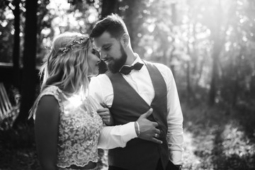 Sensual Black and white foto of bride and groom. Stylish couple of happy newlyweds posing in the park on their wedding day. Handsome bearded groom admires and kisses pretty bride. Together.