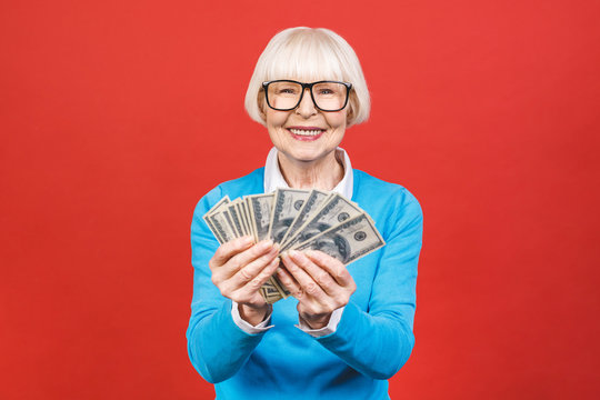 Image of mature senior happy old woman standing isolated over red background wall looking camera holding money.