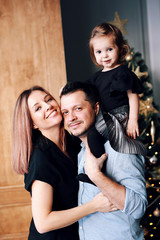 Beautiful big family smiling, hugging. Young happy parents with their little daughter having fun together near the Christmas tree