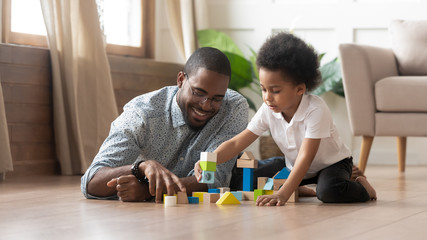 African father and son play with toy blocks on floor
