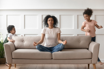 While noisy kids running young african mother meditates on couch