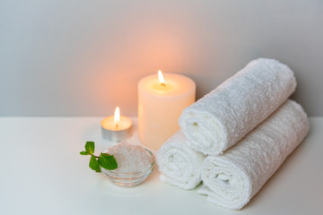 Obraz na płótnie Canvas SPA procedure at salon concept photo on grey background with stack of white towels, candles and cup of sea salt.