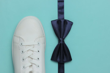 Obraz premium Minimalistic fashion still life, groom look. Stylish white sneakers and a bow tie on blue background. Top view