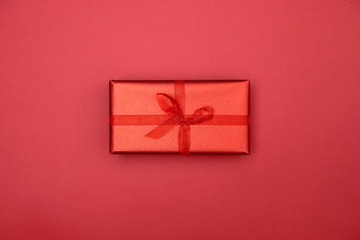 Red gift box with ribbon bow on red background, copy space. Christmas texture. Minimalism concept. Top view, flat lay. Mothers day, birthday, Women's Day, Valentine's day, Wedding, Anniversary