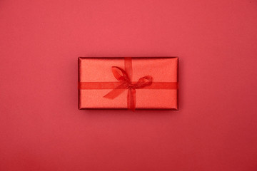 Red gift box with ribbon bow on red background, copy space. Christmas texture. Minimalism concept. Top view, flat lay. Mothers day, birthday, Women's Day, Valentine's day, Wedding, Anniversary