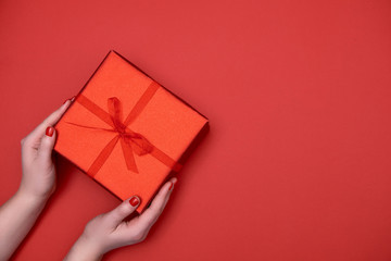 Close up of woman hands holding red gift box on red background, copy space. Christmas, New Year, Mothers day, birthday, Women's Day, Valentine's day concept. Flat lay, top view