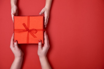 Mother giving christmas gift to son on red background, copy space. Holidays, childhood concept. Close up of child and mother hands with gift box. Top view, flat lay. Mothers day