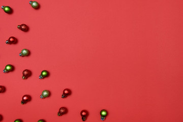Creative Christmas pattern with red and green shiny baubles on red background, copy space. Minimal, winter, new year concept. Top view, flat lay