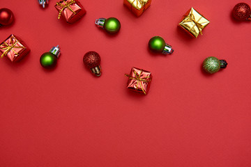 Creative Christmas pattern with red and green shiny baubles and gifts on red background, copy space. Minimal, winter, new year concept. Top view, flat lay