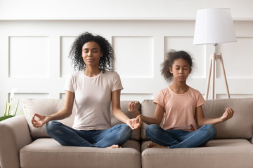 African mother and daughter practises yoga on couch at home