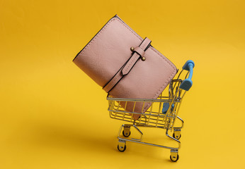 Minimalistic shopping concept. Mini shopping trolley with wallet on a yellow background