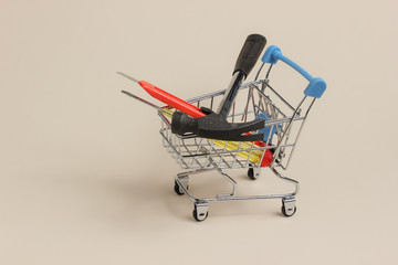 Service concept, shopping. Mini shopping trolley with hammer, screwdriver, knife on a beige background.