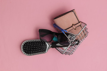 Minimalistic shopping concept. Mini shopping basket with female accessories on pink pastel background