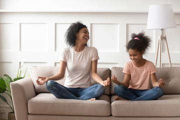 African mother daughter distracted from meditation laughing sitting on couch
