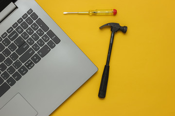 Service center, laptop repair. Laptop, screwdriver and hammer on yellow background. Top view