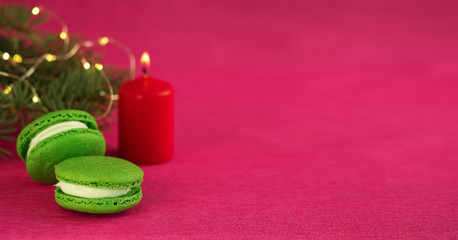 Green macaron with fondant on red paper background. Nearby is a Christmas tree branch with a...
