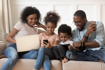 African family and kids using different gadgets sitting on couch
