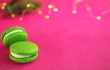 Green macaron with fondant on red paper background. Near a branch of a Christmas tree with a garland. Close-up, copy space for text. Postcard or banner concept.
