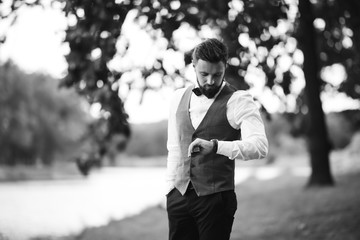 Black and white portrait of confident handsome man in black suit with bowtie posing in the park. Luxury groom in suit. Businessman. Happy smiling groom newlywed. Rich man at wedding day. 