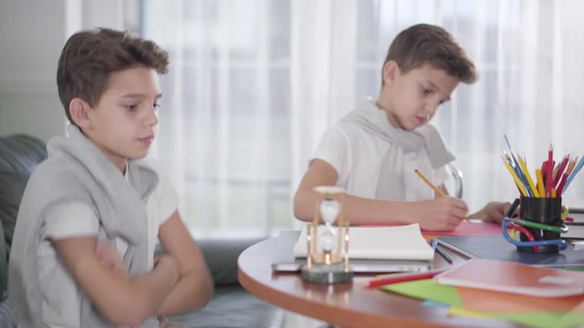 Side view of little Caucasian boy waiting for twin brother to drawing the picture and giving high five. Smart siblings doing homework together at home. Generation Z, bright mind, education concept.