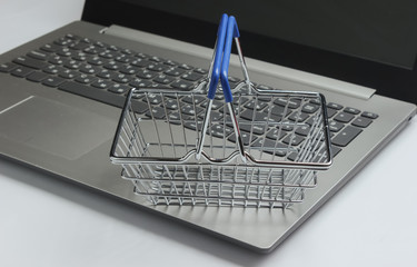 Online shopping concept. Laptop and mini shopping basket on white background