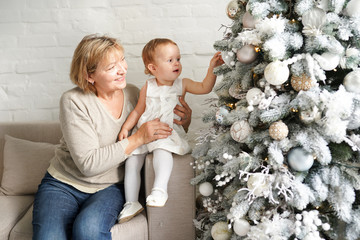 christmas family, grandmother and baby girl sitting near christmas tree on the sofa, holiday concept