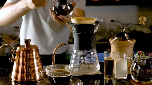 Hand drip coffee, Barista making drip coffee by pouring spills hot water on coffee ground with prepare filter from copper  teapot to glass transparent chrome drip maker. on wooden table cafe shop.
