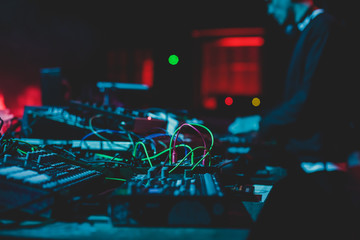 View of Dj mixer and vinyl plate with headphones on a table with DJ playing and mixes the track in the background, during night techno party in the nightclub - obrazy, fototapety, plakaty