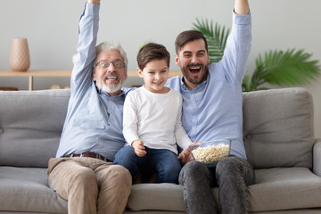 Happy grandfather, father and little son watching tv together