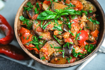 Vegetable saute or caponata, or pisto with eggplant, peppers, tomatoes and herbs in rustic bowl on a dark background.