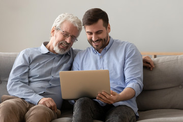 Smiling old father and adult son looking at laptop screen