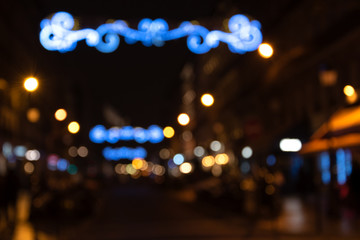 Blurry photo of Parisian street at night in center city decorated with beautiful Christmas lights decoration. Winter holidays vacation and travel in Europe  concept. Festive urban blurry background.